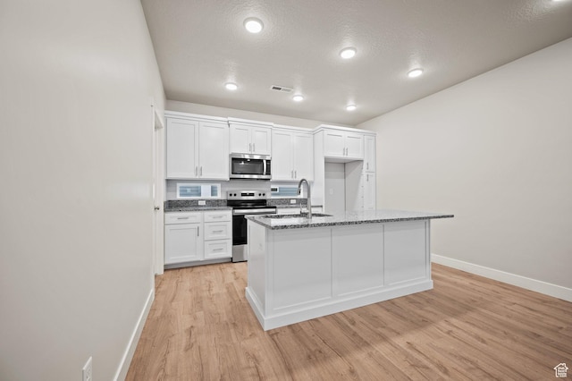 kitchen with stainless steel appliances, baseboards, light wood finished floors, white cabinets, and dark stone countertops