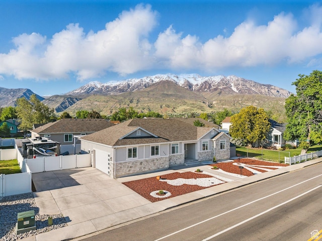 single story home with stone siding, fence, a garage, concrete driveway, and a mountain view