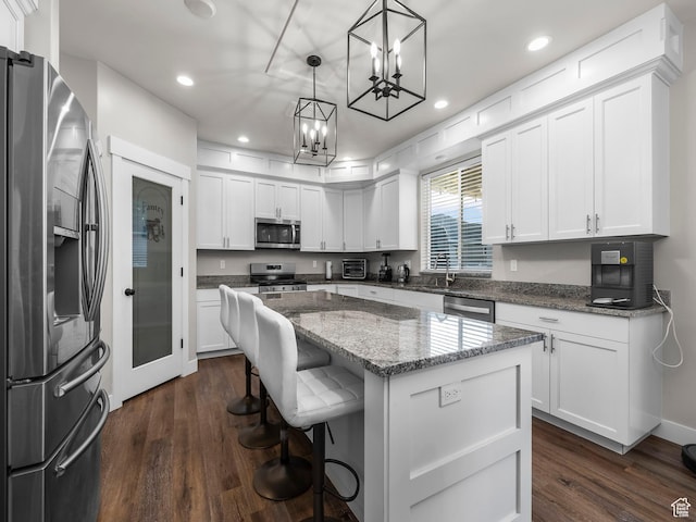 kitchen with appliances with stainless steel finishes, a chandelier, dark wood-type flooring, a center island, and white cabinetry