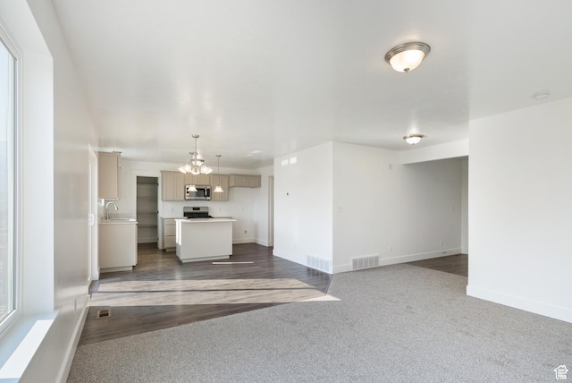 unfurnished living room featuring a chandelier, a sink, baseboards, and dark colored carpet