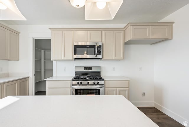 kitchen featuring appliances with stainless steel finishes, baseboards, dark wood finished floors, light countertops, and cream cabinets