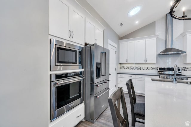 kitchen with appliances with stainless steel finishes, lofted ceiling, wood finished floors, tasteful backsplash, and white cabinetry