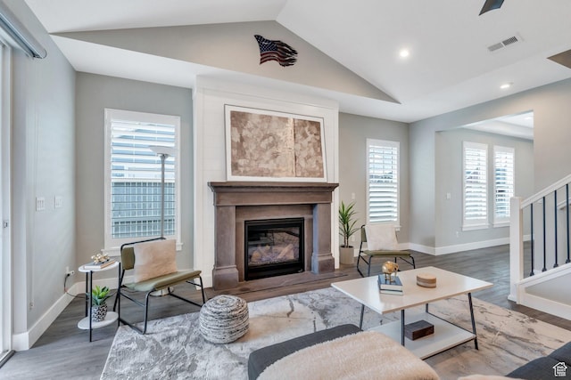 living area featuring lofted ceiling, wood finished floors, a glass covered fireplace, baseboards, and recessed lighting