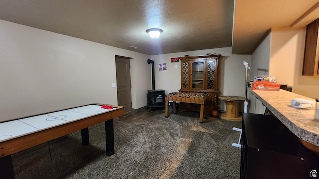 rec room featuring a wood stove, dark colored carpet, and a textured ceiling