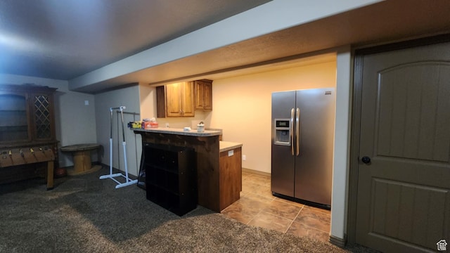kitchen with stainless steel fridge with ice dispenser, a peninsula, light countertops, light carpet, and brown cabinets