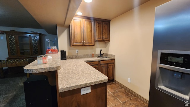 kitchen featuring a sink, a peninsula, light countertops, baseboards, and dark tile patterned flooring