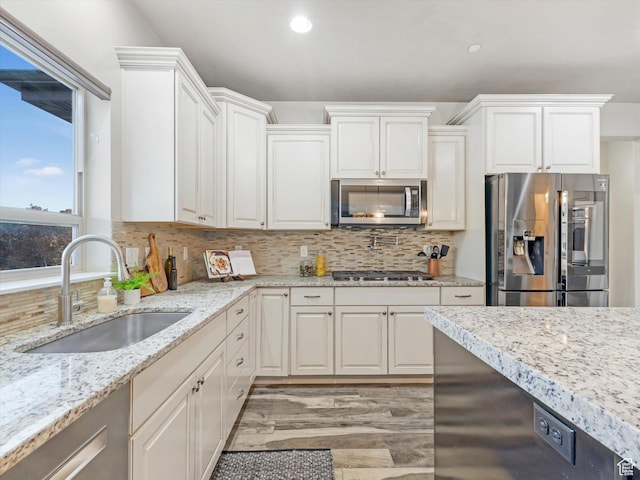 kitchen with appliances with stainless steel finishes, a sink, tasteful backsplash, white cabinetry, and light wood finished floors