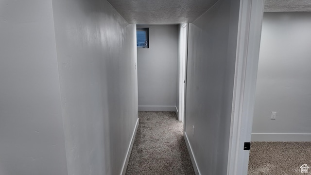 hall featuring a textured ceiling, carpet, and baseboards