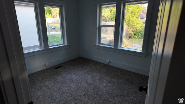 empty room featuring plenty of natural light and dark carpet