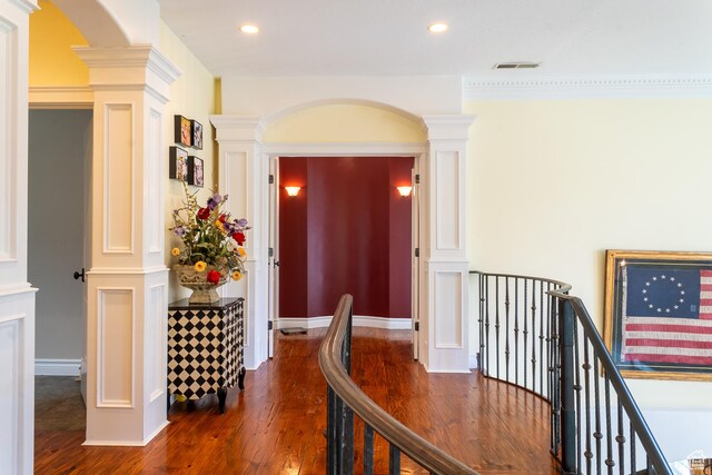 hall with decorative columns, dark wood-style floors, an upstairs landing, arched walkways, and recessed lighting