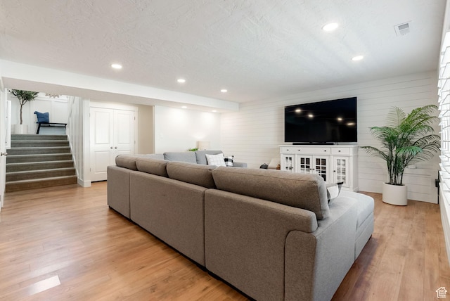 living area featuring stairs, light wood-style flooring, recessed lighting, and wooden walls