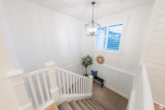 staircase featuring a wainscoted wall, a chandelier, a decorative wall, and carpet floors