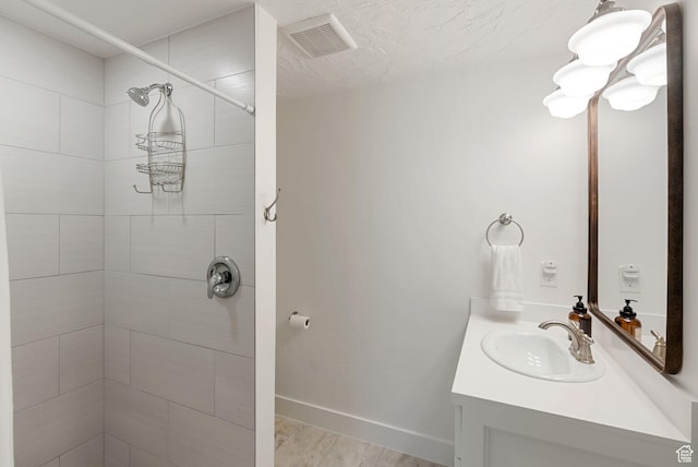 bathroom with tiled shower, vanity, and baseboards