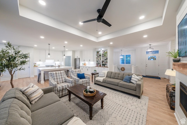 living room featuring a ceiling fan, light wood-type flooring, recessed lighting, a tray ceiling, and a fireplace