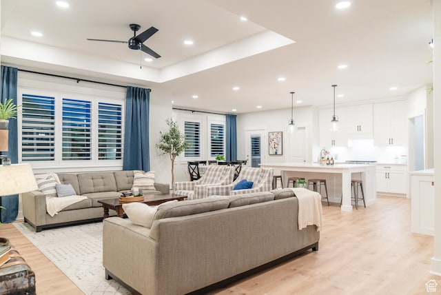 living area featuring a ceiling fan, light wood-style floors, recessed lighting, and a tray ceiling