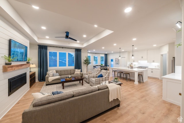 living room with light wood finished floors, a raised ceiling, a fireplace, a ceiling fan, and recessed lighting