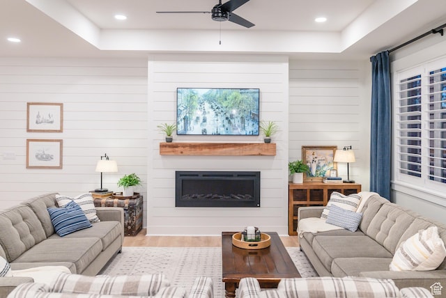 living room featuring a ceiling fan, wood finished floors, a fireplace, recessed lighting, and a tray ceiling