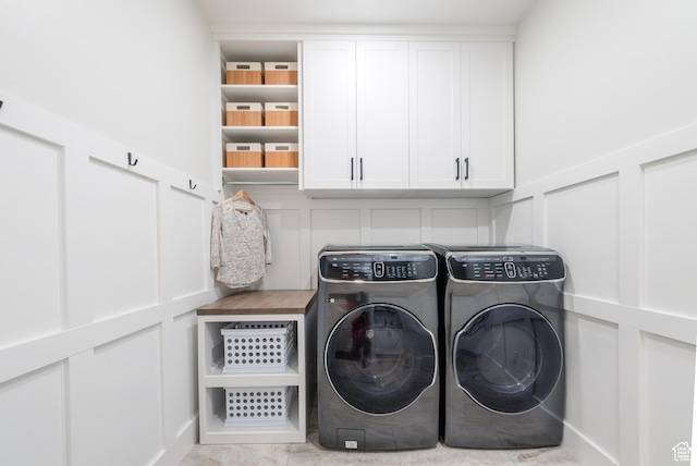 clothes washing area featuring a decorative wall, washer and dryer, and cabinet space