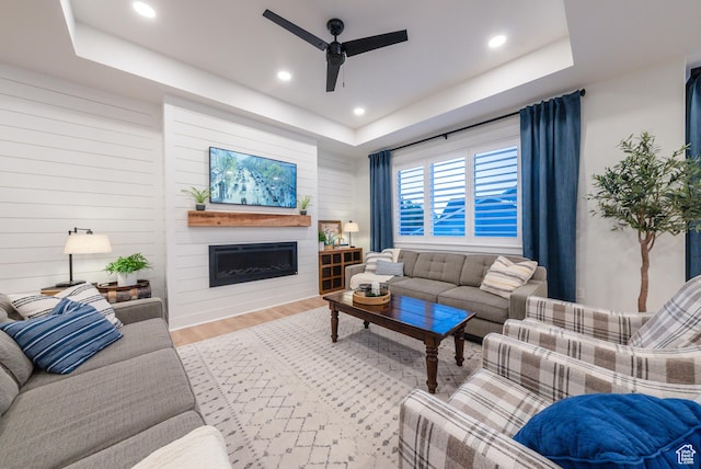 living room with a raised ceiling, a ceiling fan, wood finished floors, a fireplace, and recessed lighting
