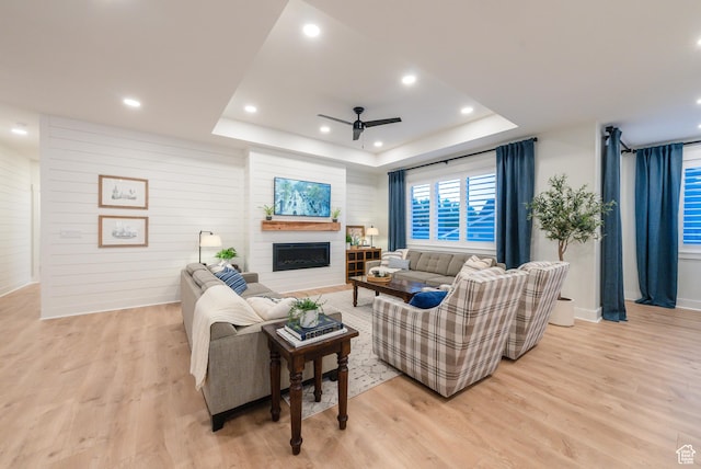 living room with a tray ceiling, ceiling fan, light wood-type flooring, a fireplace, and recessed lighting