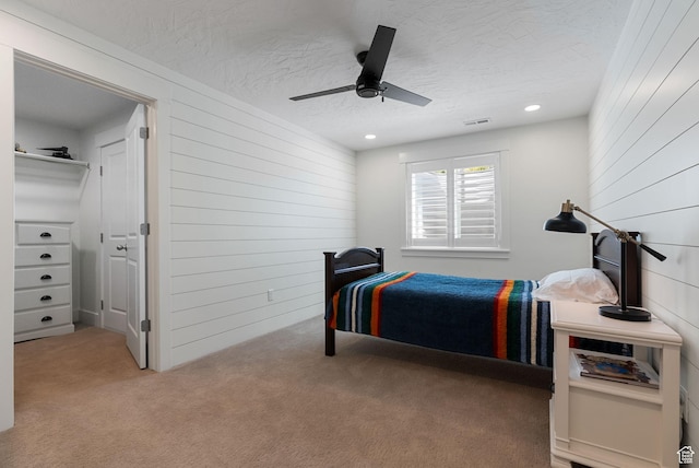 carpeted bedroom with wooden walls, a textured ceiling, a ceiling fan, and recessed lighting