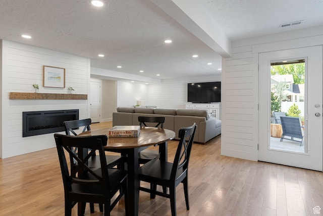 dining space featuring light wood-type flooring, a textured ceiling, a glass covered fireplace, and recessed lighting