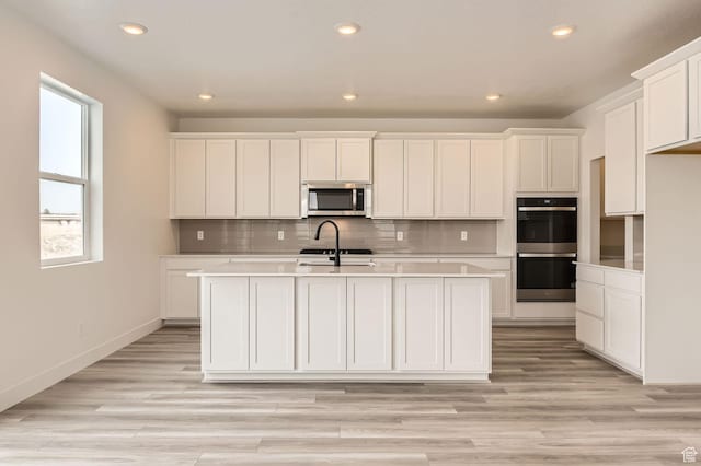 kitchen featuring appliances with stainless steel finishes, recessed lighting, a center island with sink, light countertops, and white cabinetry