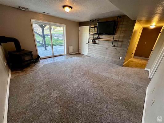 1204 Nashua Cir, Soda Springs, ID 83276 - unfurnished living room with a wood stove, a textured ceiling, carpet floors, and baseboards
