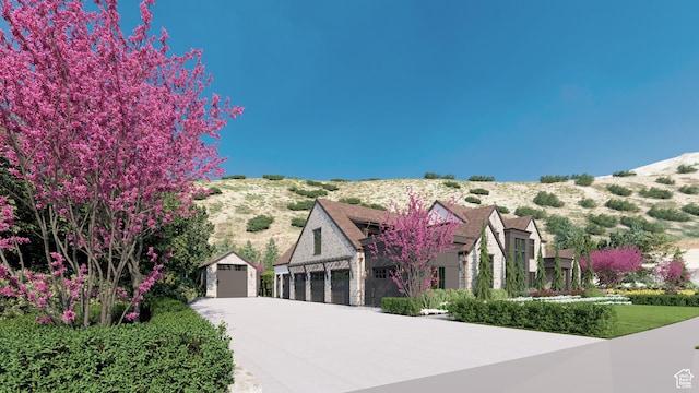 view of front of property featuring concrete driveway, a mountain view, an outbuilding, and stone siding