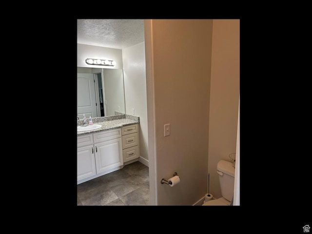 bathroom with a textured ceiling, toilet, vanity, and baseboards