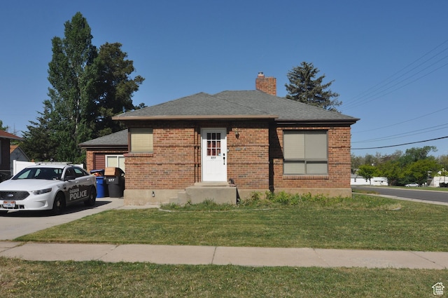 view of front of home with a chimney, a front yard, brick siding, and a shingled roof