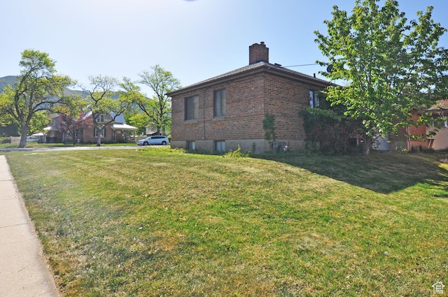 view of side of home with a chimney, brick siding, and a lawn