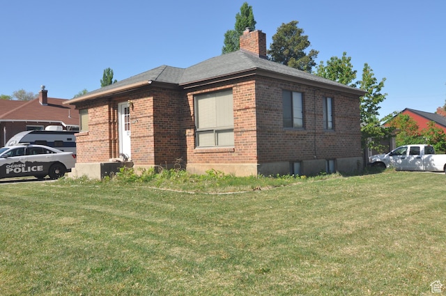 view of side of home featuring brick siding, a yard, and a chimney