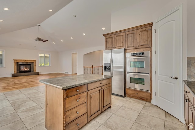 kitchen featuring stainless steel appliances, ceiling fan, light tile patterned floors, a center island, and vaulted ceiling