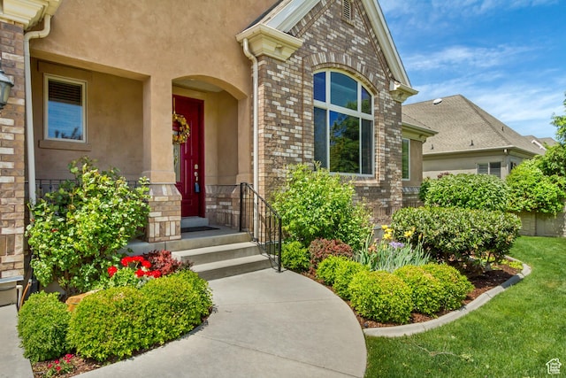 view of exterior entry with stucco siding, stone siding, and brick siding