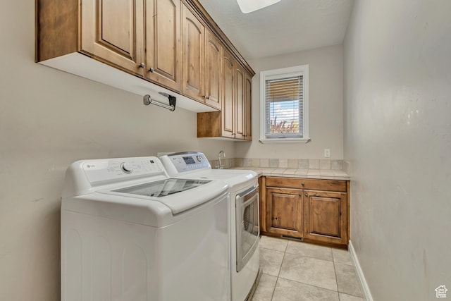 clothes washing area featuring cabinet space, separate washer and dryer, light tile patterned floors, and baseboards