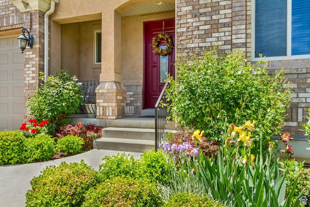 entrance to property with covered porch, a garage, stone siding, and stucco siding