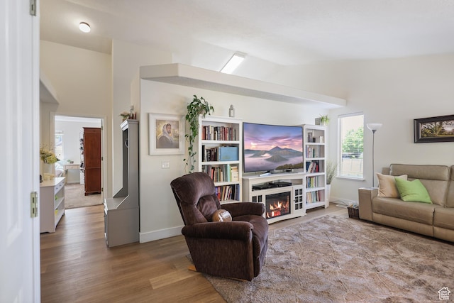 living room with lofted ceiling, wood finished floors, a glass covered fireplace, and baseboards