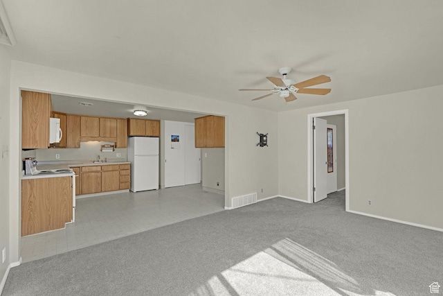 unfurnished living room featuring a sink, a ceiling fan, baseboards, and light colored carpet