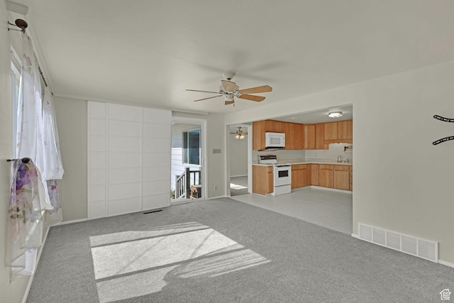 unfurnished living room with a ceiling fan, light colored carpet, and healthy amount of natural light