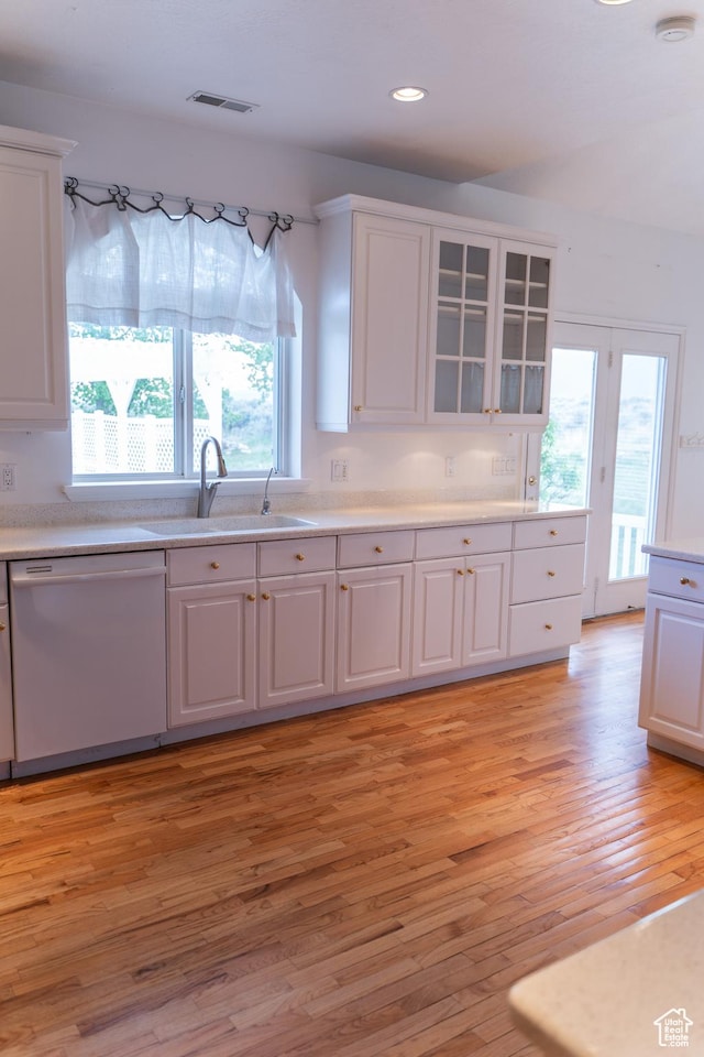 kitchen with white dishwasher, a sink, white cabinets, light wood-style flooring, and light countertops