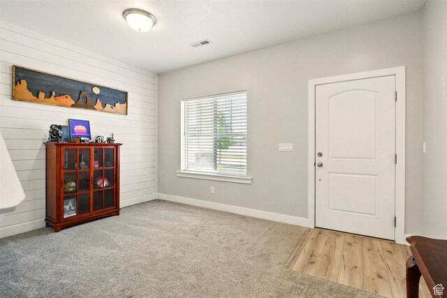 carpeted entrance foyer with baseboards and wood walls