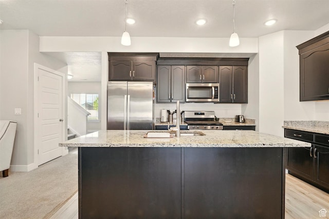 kitchen featuring stainless steel appliances, a sink, light stone countertops, a center island with sink, and dark brown cabinets