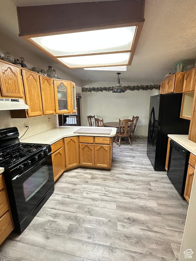 kitchen featuring black appliances, a peninsula, under cabinet range hood, light wood finished floors, and light countertops