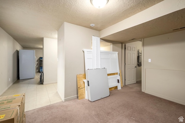 basement with a textured ceiling, baseboards, freestanding refrigerator, and light colored carpet