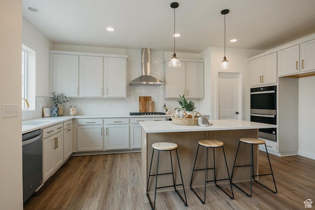 kitchen featuring wall chimney range hood, double wall oven, stainless steel dishwasher, a kitchen island, and a kitchen bar
