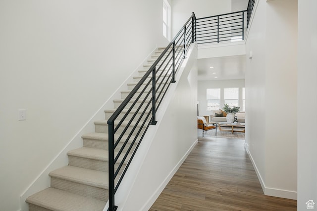 stairway featuring baseboards, wood finished floors, and a high ceiling