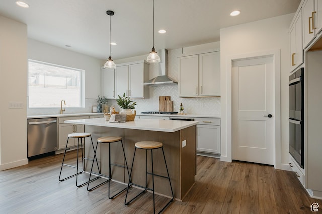 kitchen featuring dishwasher, wall chimney exhaust hood, a breakfast bar, wood finished floors, and a center island