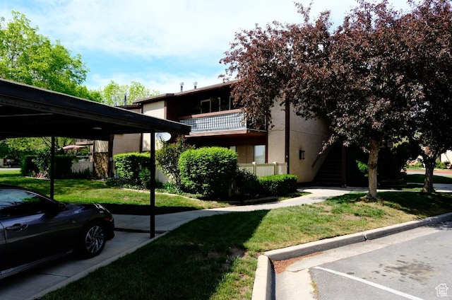 view of front facade with a front yard, a parking lot, stucco siding, and stairway