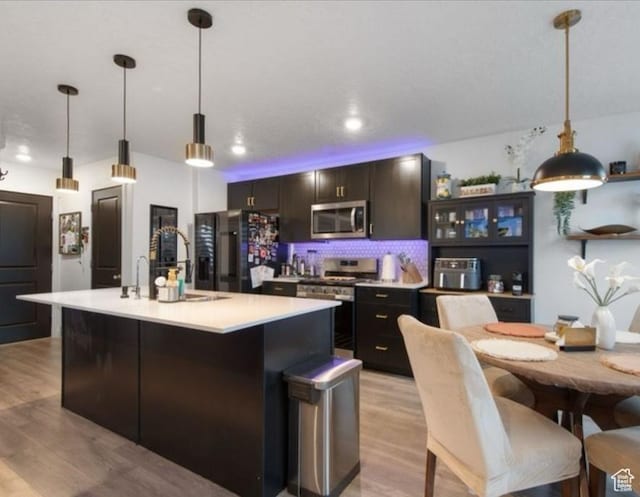 8578 W Bowie Dr, Magna, UT 84044 - kitchen with appliances with stainless steel finishes, light wood-type flooring, an island with sink, light countertops, and backsplash